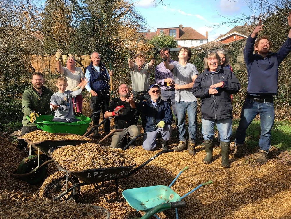 Volunteers posing for a group photo by pile of woodchip