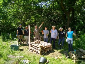 Volunteers posing for a group photo behind the beginnings of the bug hotel